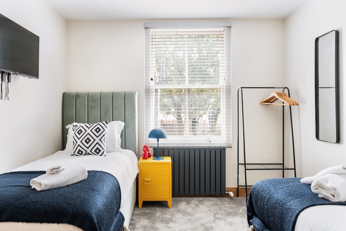 Alójate en este vibrante apartamento en el corazón de Londres, con un acogedor dormitorio con dos cómodas camas individuales, un televisor montado en la pared y un armario abierto para un espacio elegante y funcional, perfecto para una escapada a la ciudad.