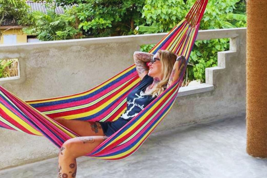 A colorful striped hammock is suspended on a spacious terrace, surrounded by lush greenery. The hammock offers a relaxing space to unwind, with ample light filling the area, creating an inviting atmosphere for guests to enjoy.