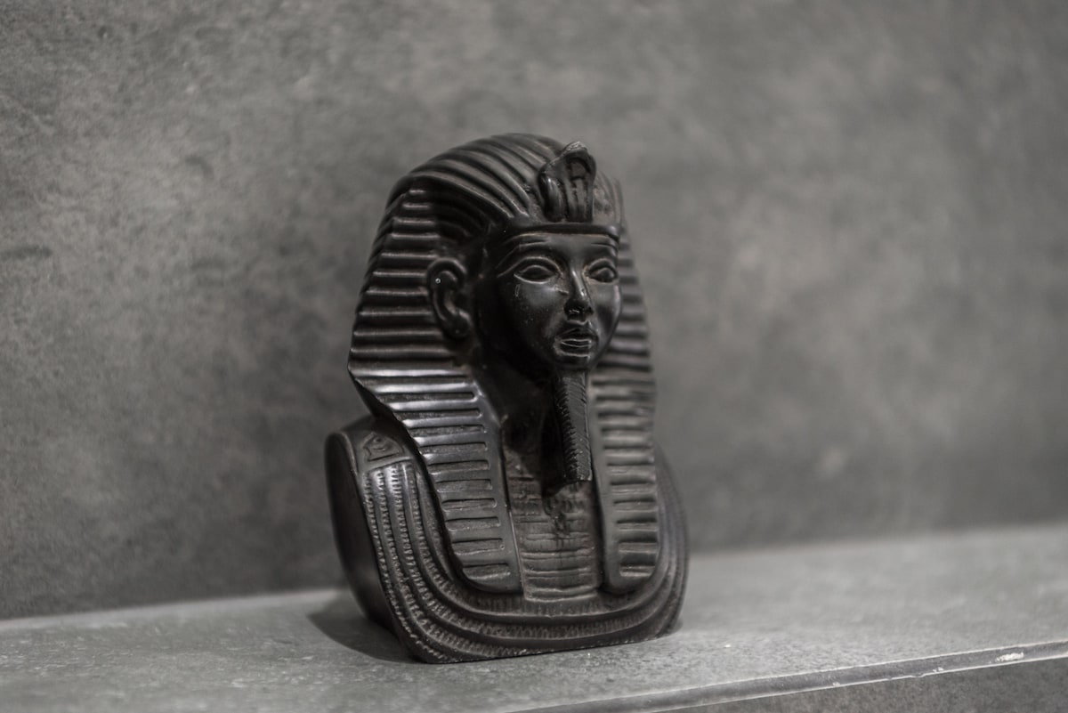A decorative black statue resembling an ancient Egyptian figure is displayed on a smooth, grey countertop. The intricate detailing of the statue reflects a historical design, contributing a unique artistic touch to the space.