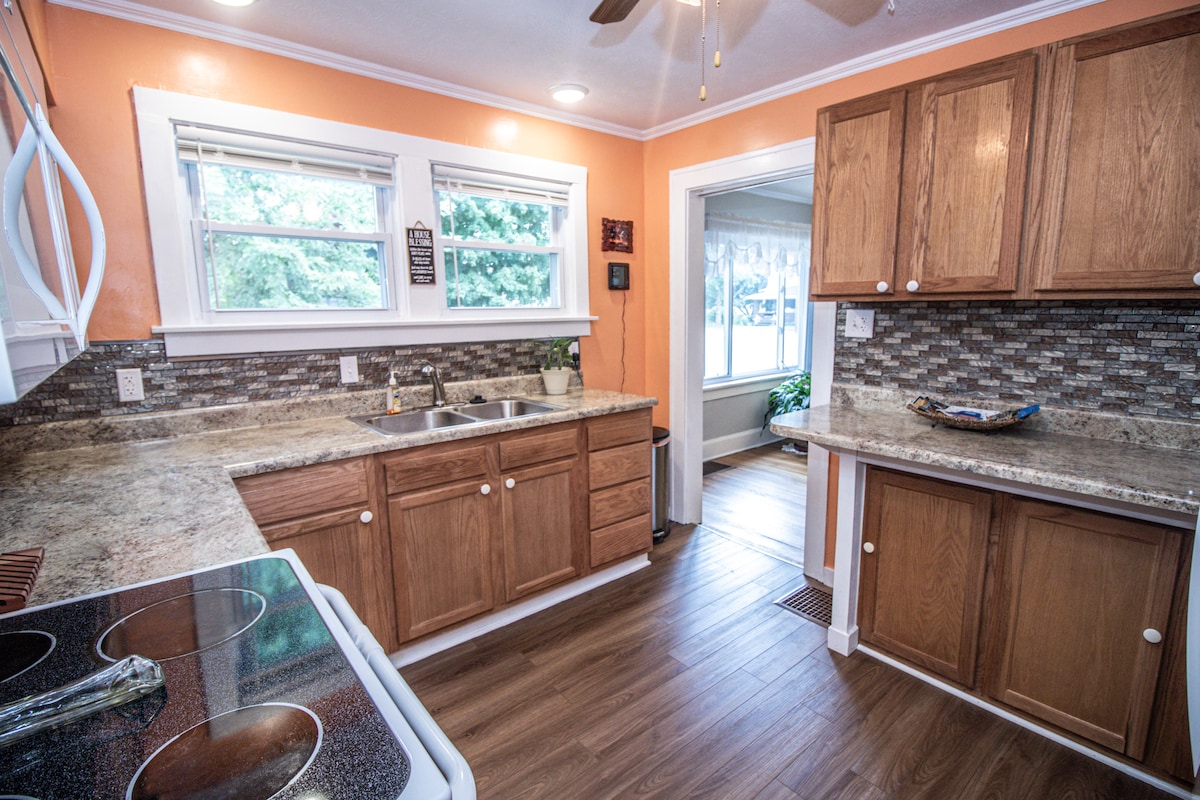 The kitchen features wooden cabinetry and a granite countertop. A sink is situated beneath a window, allowing natural light. The floor is finished in a wood-like style. Appliances include a stove and ample counter space, creating a functional cooking area.