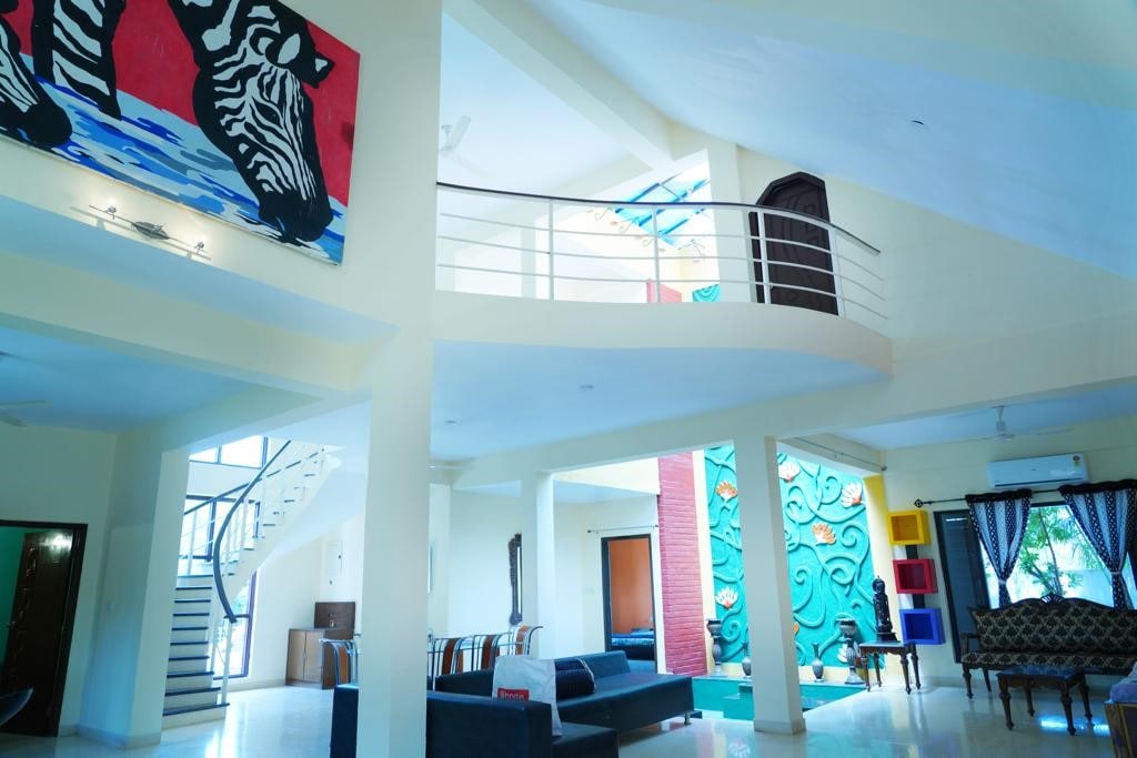 An open-plan living area showcases a bold zebra artwork on the wall. A spiral staircase leads to the upper level, while large windows provide ample natural light. The furniture arrangement includes a dark sofa and a stylish table, blending comfort with modern design.