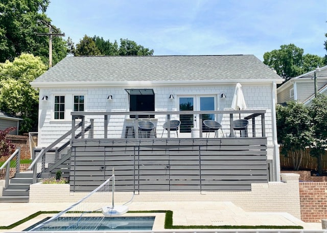 A studio pool house is shown with a spacious deck featuring several outdoor chairs. Large windows provide views of the backyard and pool area. Lush greenery surrounds the property, adding to the sense of privacy and relaxation.