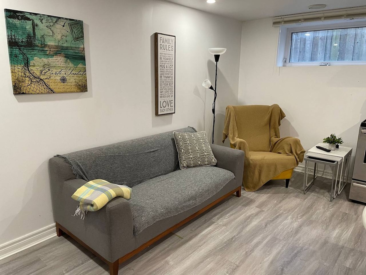 A comfortable seating area is provided, featuring a gray sofa accompanied by a cozy armchair draped with a tan throw. A modern floor lamp stands beside the couch, while a small table holds decorative items. Wall art adds personality to the inviting space.