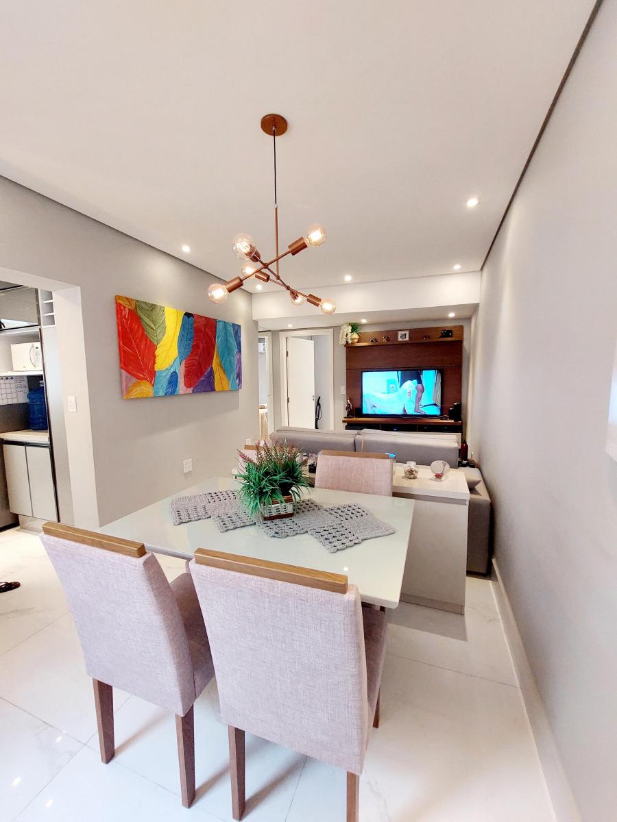 A modern dining area is depicted with a rectangular glass table surrounded by four upholstered chairs. A colorful abstract painting adorns the wall, while a smart TV is visible in the background, highlighting the living space's openness and contemporary design.