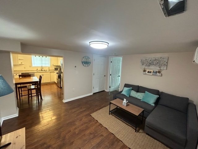 A cozy living area features a dark sectional sofa adorned with turquoise accents. Natural light filters through a nearby window, illuminating the hardwood floor. A small coffee table sits in front of the couch, complementing the relaxed atmosphere of the space.