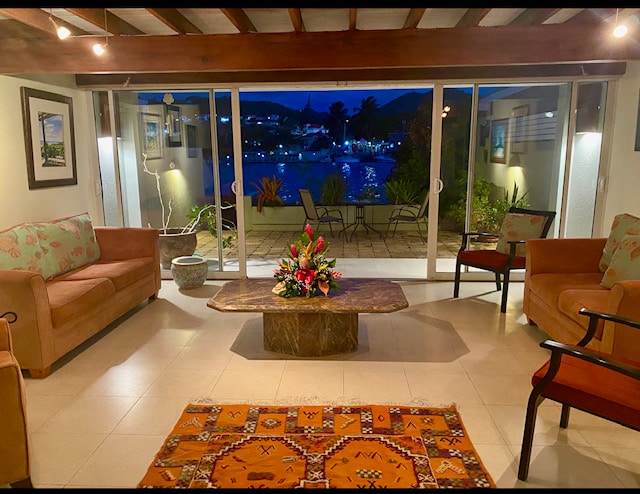 A spacious living area features two comfortable couches facing a coffee table with a floral arrangement. Large sliding glass doors offer views of the patio and marina, while warm lighting illuminates the room. A colorful area rug adds a touch of character to the tiled floor.