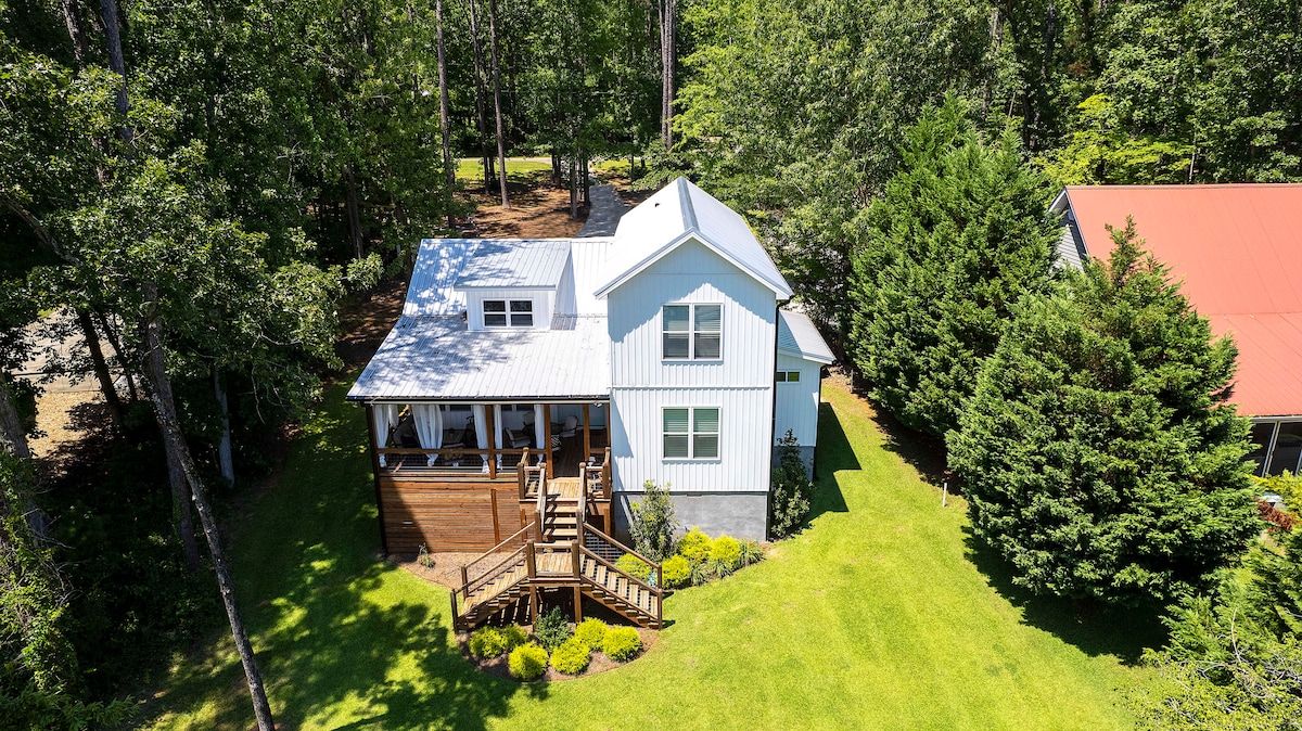 An aerial view of the home reveals a two-story structure surrounded by greenery. The exterior features a light blue facade with a welcoming porch and steps leading to the entrance. Nearby trees and manicured grass provide a serene outdoor setting.