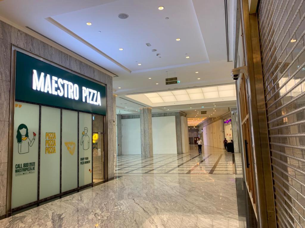 A modern corridor is visible, featuring polished marble flooring and high ceilings. The entrance to Maestro Pizza is prominently displayed on the left, with large glass windows showcasing the brand's logo. The ambiance is well-lit, contributing to a spacious and welcoming atmosphere.