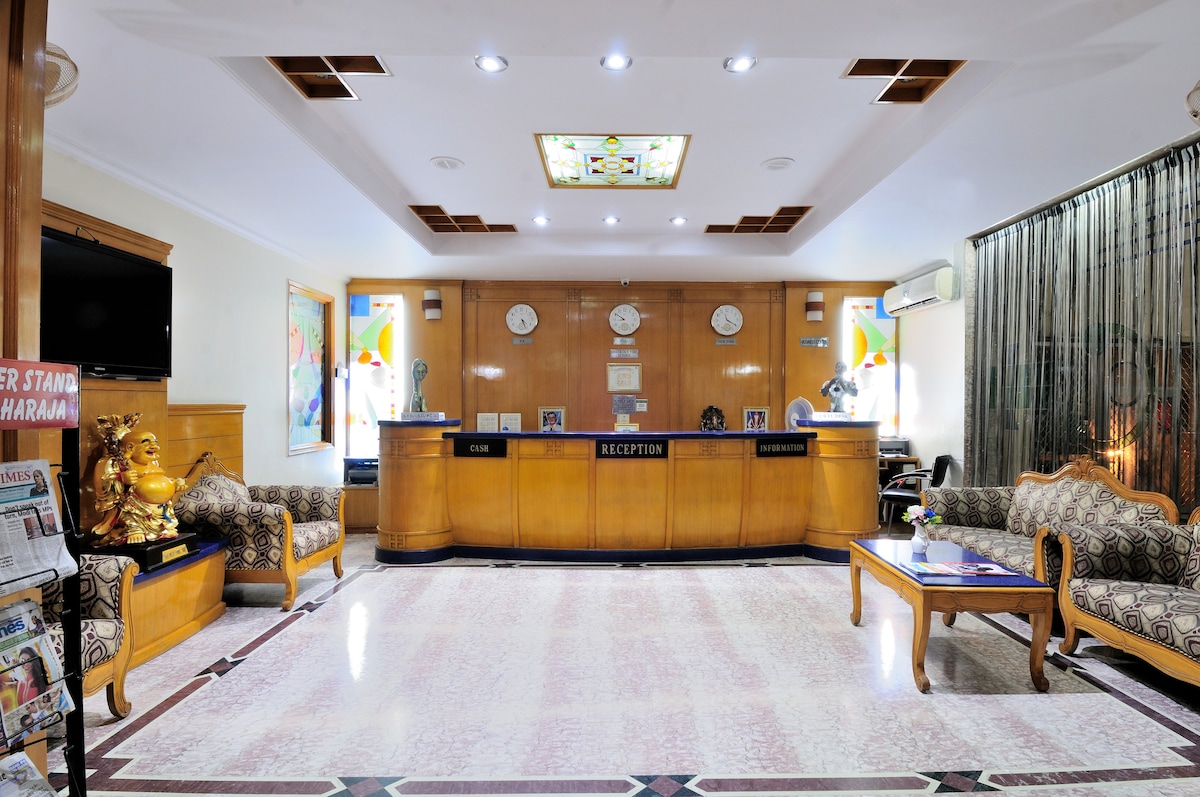 The reception area features a polished marble floor and a wooden reception desk. Wall clocks of various designs are displayed above the desk, while comfortable seating arrangements are provided with patterned upholstery. Illuminated panels accentuate the space, enhancing its welcoming ambiance.