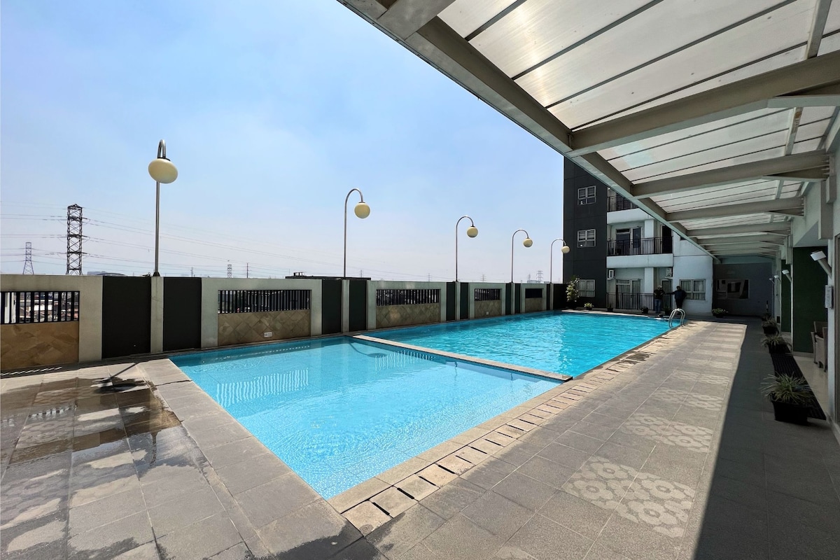An outdoor swimming pool is visible, surrounded by a sleek tiled area. Modern lamp posts are positioned along the pool's edge, offering lighting. A clear sky hangs above, complementing the tranquil atmosphere of the space.