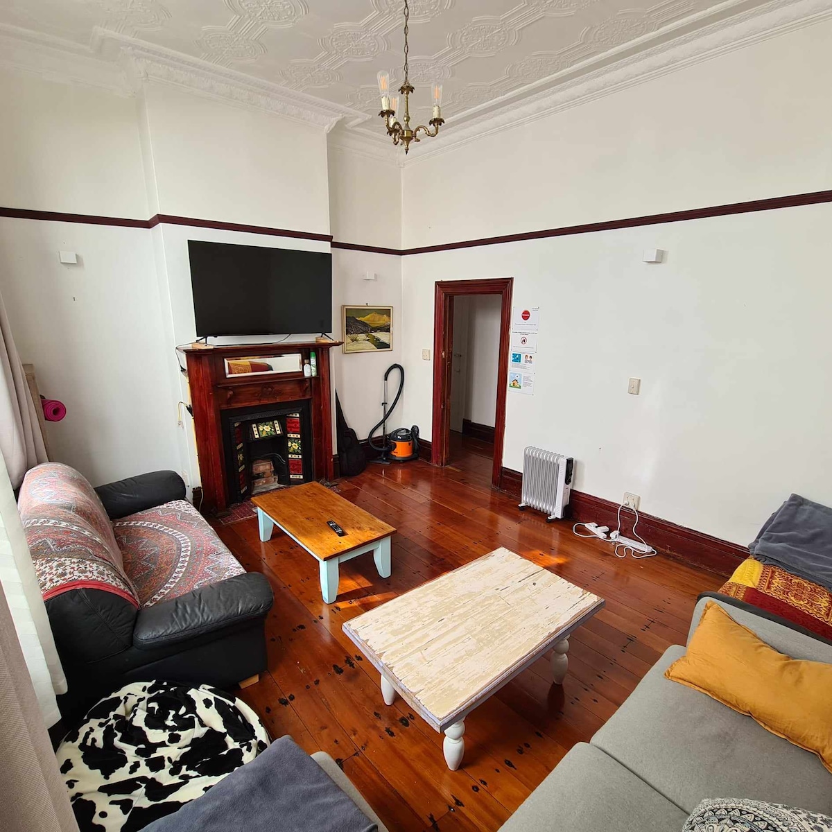 The lounge area features a combination of seating options, including a dark sofa and a light-colored couch, arranged around a coffee table. A television is mounted on the wall, and a decorative fireplace is present. Hardwood floors and elegant moldings contribute to the room's character.