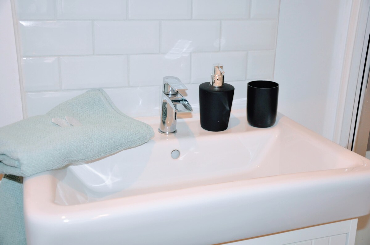 A modern sink displays a chrome faucet and a minimalist design. A soft blue towel is neatly folded nearby. Two black containers, one for soap and the other for accessories, are positioned beside the faucet, adding a touch of elegance to the space.