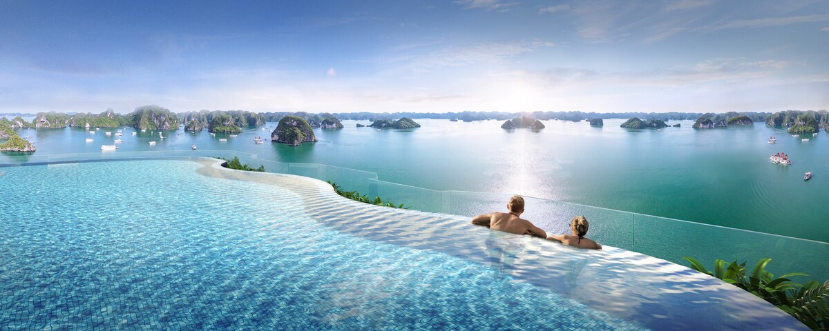 An infinity pool offers breathtaking views of a serene body of water, dotted with lush green islands. The sun illuminates the horizon, creating a peaceful atmosphere for relaxation.