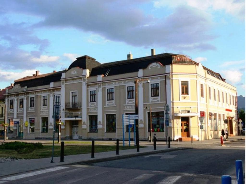 The exterior of Hotel EUROPA presents a classic architectural style with decorative elements. Large windows and a prominent entrance contribute to its elegant facade. Surrounding features include a well-maintained pathway and lampposts, set against a backdrop of a blue sky with scattered clouds.