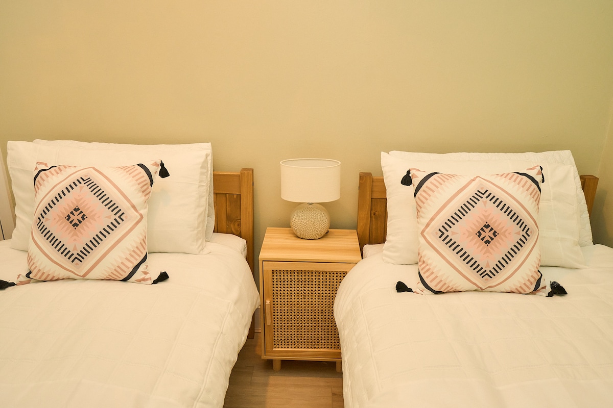 Chumba cha kulala cha mapacha angavu chenye mashuka yenye starehe, vivutio vya boho na kinara cha kupendeza.