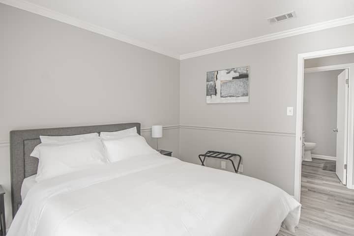Tranquil Retreat in Our Queen Bedroom – استمتع بالهدوء وأنت تستريح في سريرنا الملكي المريح. تخلق اللمسات المدروسة مثل فن الجدار الأنيق، ورف الأمتعة المريح، ومصباح السرير الدافئ، جوًا جذابًا لإقامة مريحة.