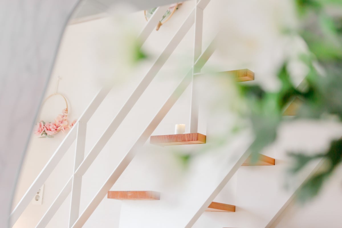 A staircase with wooden steps is visible, leading to the upper level of the home. Soft greenery and delicate flowers frame the image, creating a serene atmosphere. The walls are painted in light colors, enhancing the spacious feel of the area.