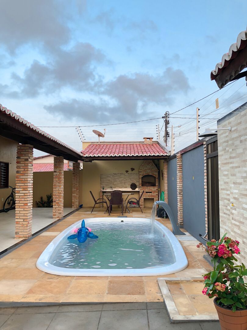 A rectangular pool is situated in a cozy courtyard, equipped with a water fountain feature. Surrounding the pool are comfortable seating arrangements, including a table and chairs. Lush potted plants add a touch of greenery, while the covered area provides shade for relaxation.