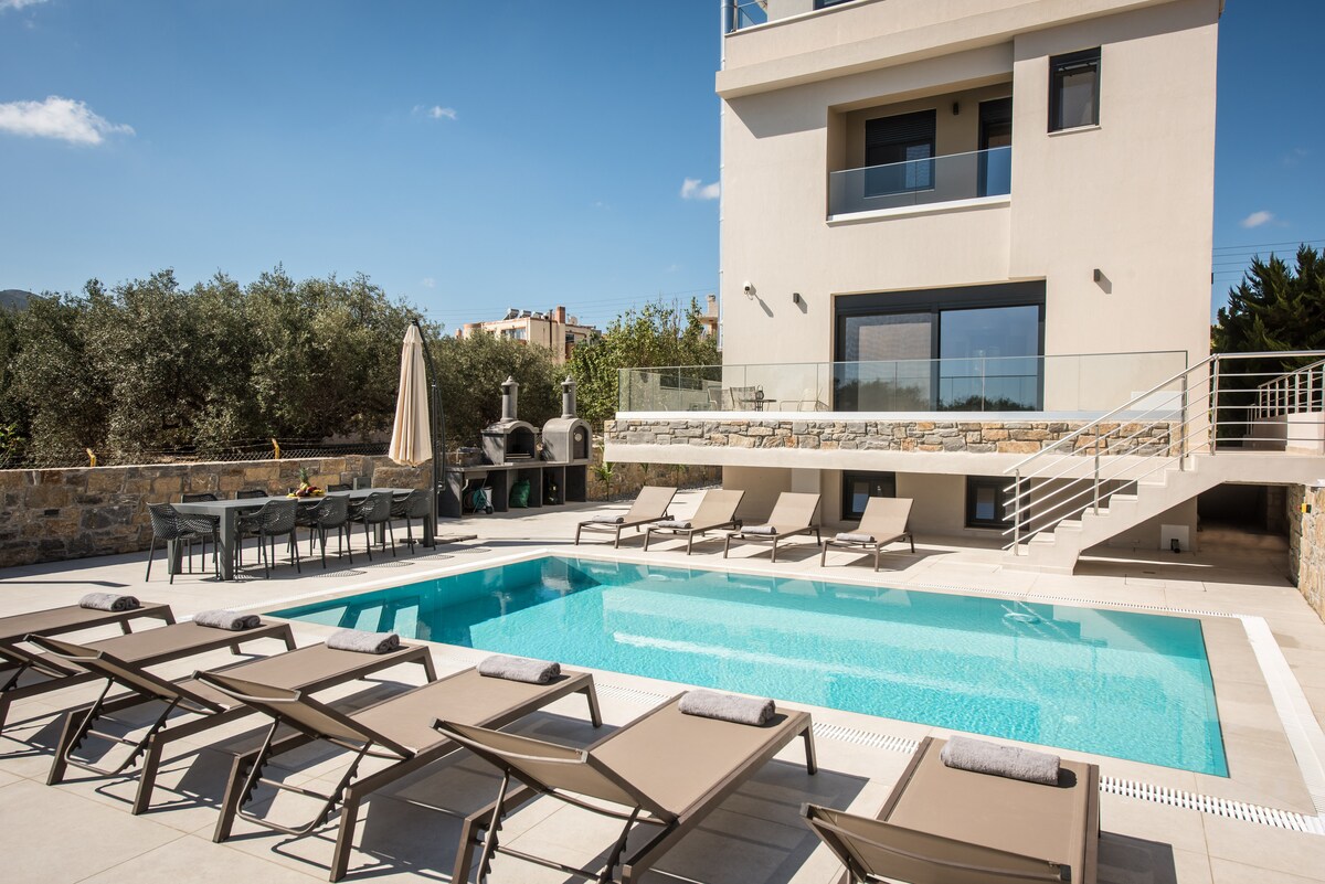 An outdoor area features a refreshing pool surrounded by several lounge chairs. A shaded dining area is seen to one side, complemented by a barbecue setup. The modern building showcases large windows, allowing natural light to flood the space.