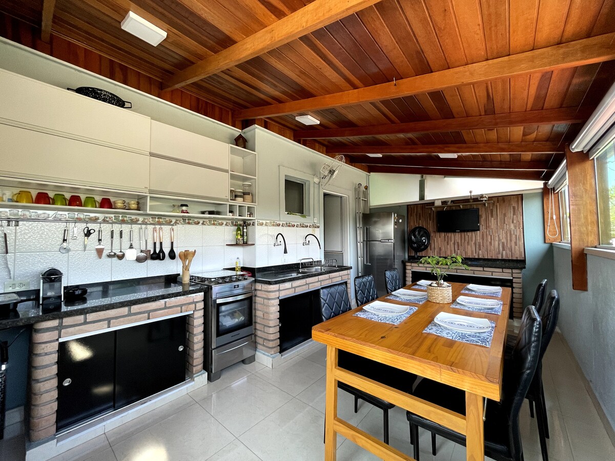The kitchen and dining area feature a modern design with wooden beams adorning the ceiling. A large wooden dining table is set for several diners, while the kitchen is equipped with black cabinets, a stove, and ample counter space, creating a functional cooking environment.