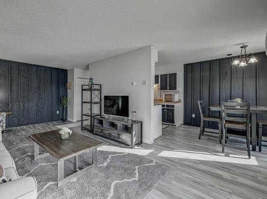 An open living area displays a light-colored sofa paired with a stylish coffee table on a soft rug. A television is mounted on a dark shelf. The dining area features a rectangular table with chairs, adjacent to a modern kitchen with wood cabinetry.