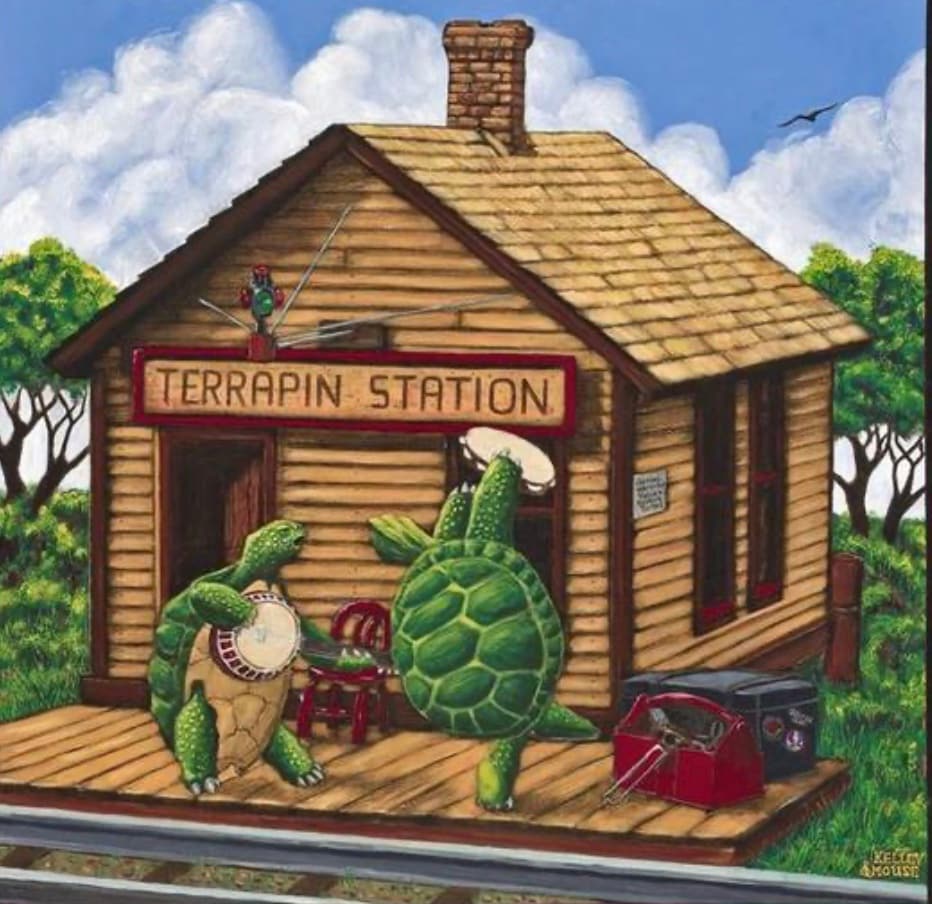 An artistic depiction of Terrapin Station features two turtles playing musical instruments on a wooden platform. The station building is characterized by a shingled roof and a welcoming porch. Lush greenery surrounds the structure, contributing to a vibrant, rural atmosphere.