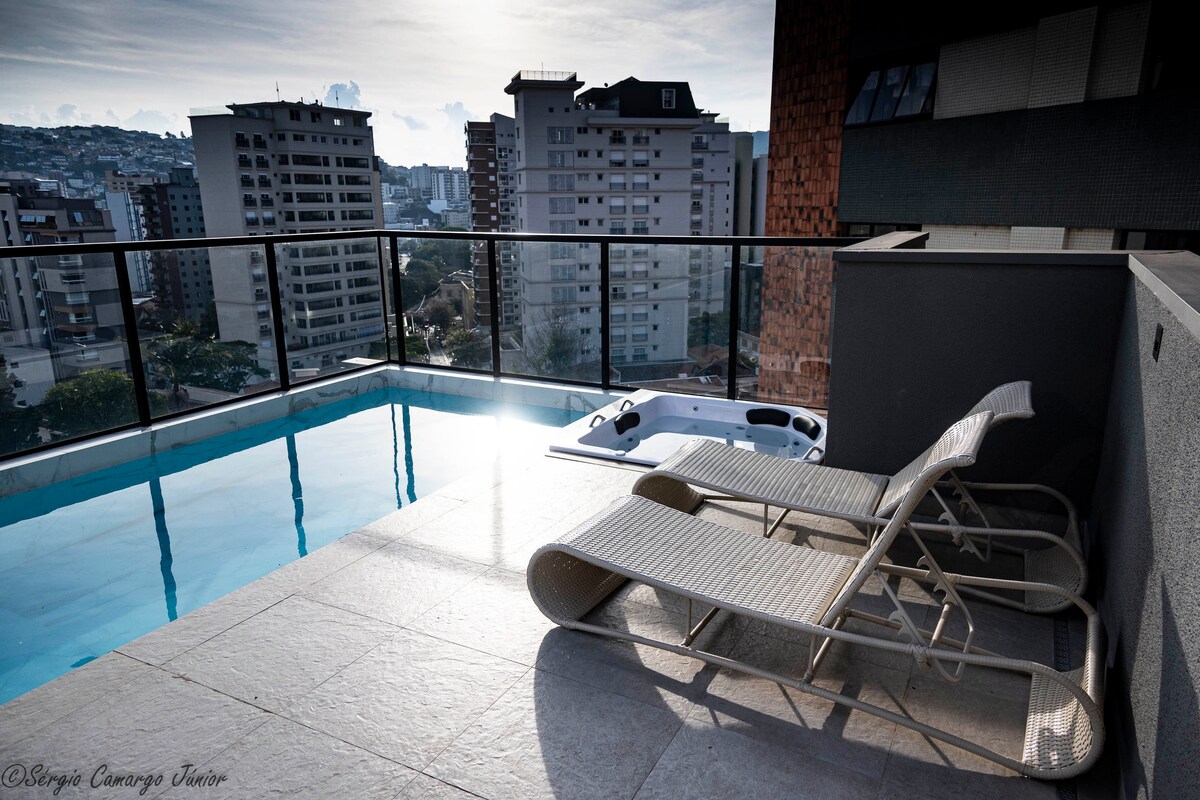 An outdoor space features a sparkling pool with a view of the city skyline. Lounge chairs are positioned beside the pool, providing a place to relax. The area is spacious and well-lit, enhancing the inviting ambiance of the rooftop.