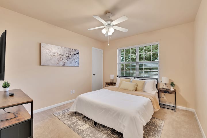 Un dormitorio acogedor con una cama tamaño queen, un televisor, una ventana para dejar entrar la luz natural y mesitas de noche para mayor comodidad y almacenamiento.