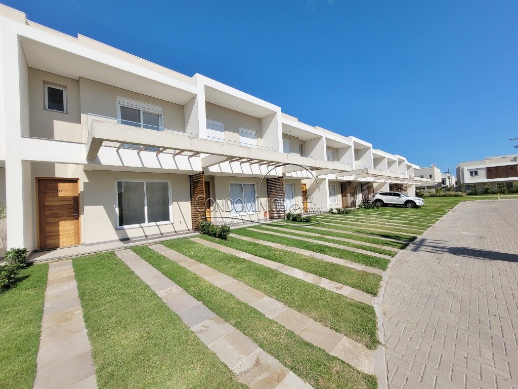 A row of modern residential units features clean lines and a minimalistic design. Each unit is complemented by a small porch area and landscaped lawns, with well-maintained greenery and a paved pathway leading through the front. A vehicle is parked in front of one of the units.