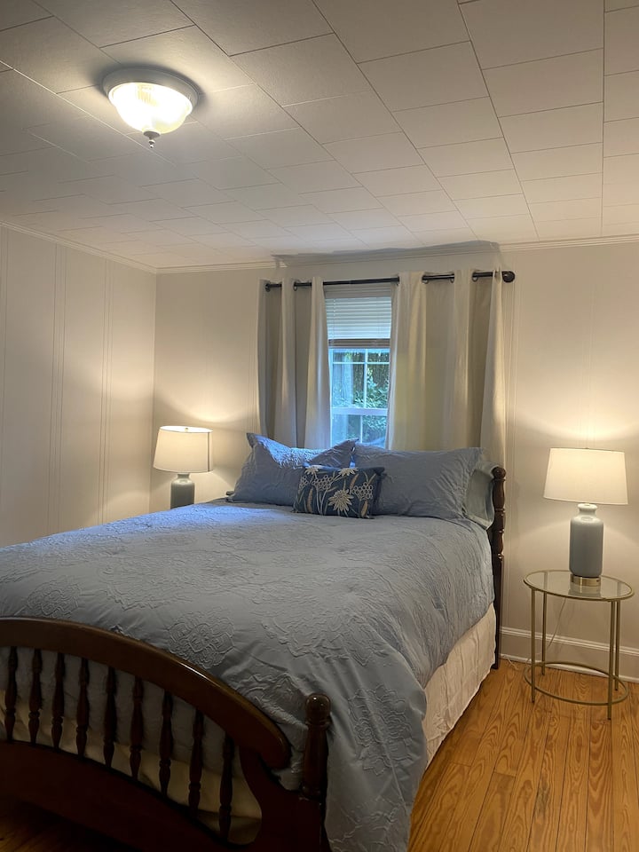 سرير مريح بمقاس كبير  مع ستائر وستائر مظلمة للغرفة على كلا النافذتين.