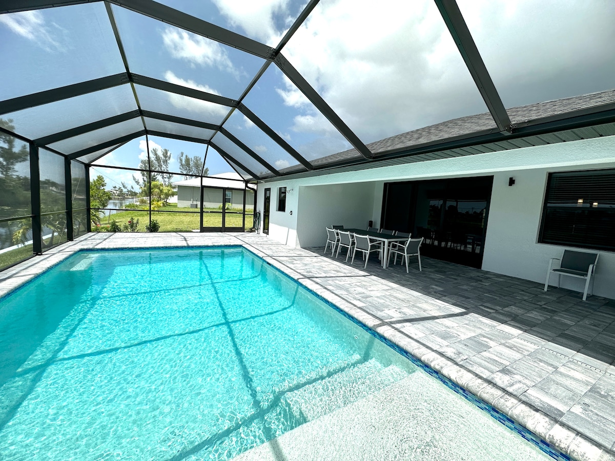 The spacious screened lanai features a crystal-clear pool, shaded seating area, and a dining table for outdoor meals. Glass panels provide unobstructed views of the surrounding greenery and sky, while the textured flooring adds a practical touch to the open space.