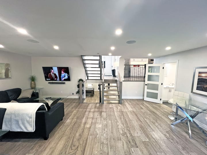 Elegant floating stairs take center stage in this bright, open-concept living space. The modern design blends seamlessly with the hardwood floors and sleek furnishings, creating a chic and inviting ambiance for your stay.