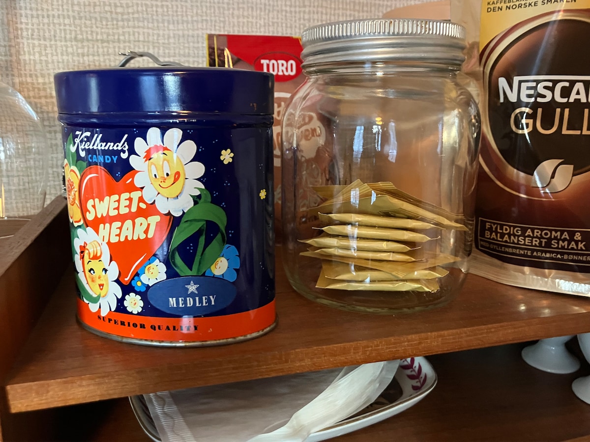 A vintage candy tin labeled 'Sweet Heart' is shown alongside a clear glass jar filled with neatly stacked packets. The colorful tin features floral designs, while the jar offers a glimpse of organized simplicity.
