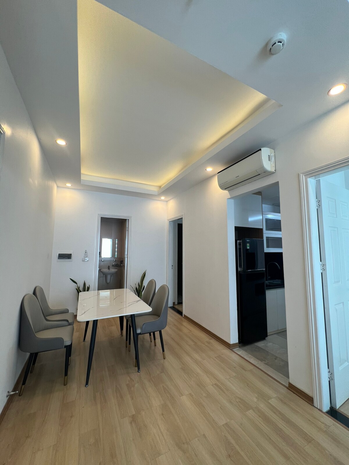 A dining area is presented with a modern table surrounded by four sleek gray chairs. The ceiling features recessed lighting that enhances the open space. Doorways lead to adjacent rooms, and light-colored flooring contributes to a bright atmosphere.