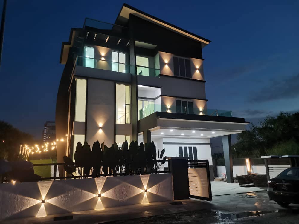The three-storey independent villa is illuminated at night, showcasing modern architectural features and large glass windows. A welcoming entrance is framed by tasteful landscaping, while warm lighting highlights the building's design and creates an inviting atmosphere.
