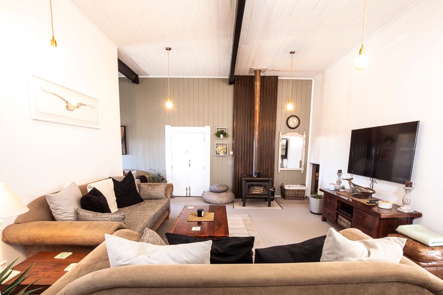 A stylish living area is presented with two large sofas adorned with cushions, facing a wooden coffee table. An elegant fireplace serves as a focal point, while a flat-screen television is mounted on the wall. Soft lighting is provided by hanging fixtures.