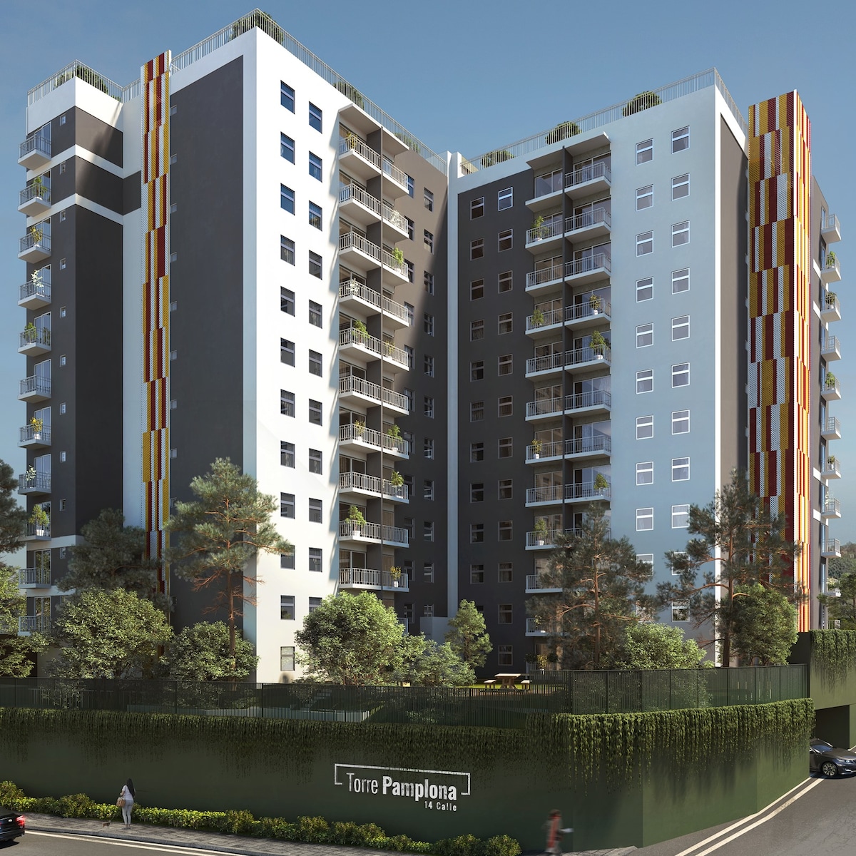 A modern multi-story building stands against a clear blue sky. The architecture features a mix of light and dark exterior colors with balconies adorned by plants. A sign reading 'Torre Pamplona 1ra Calle' is prominently displayed at the base, surrounded by green landscaping.