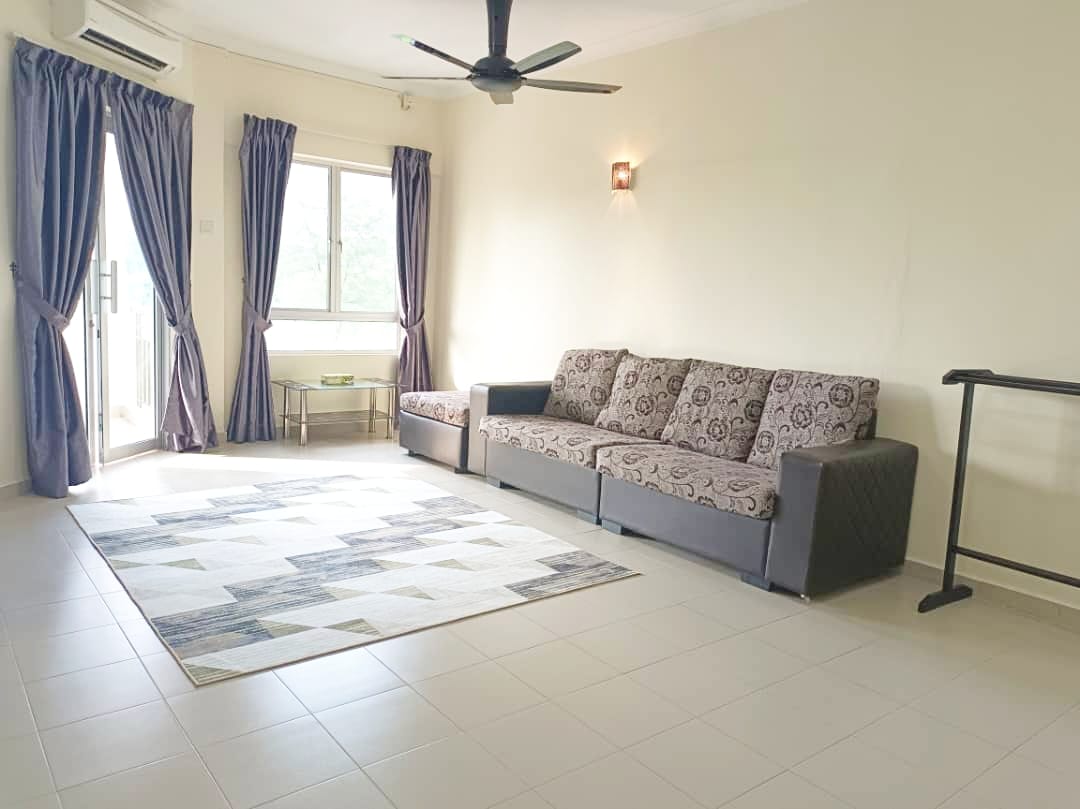 A spacious living area featuring a comfortable sofa set and a large area rug with geometric patterns. Natural light filters through the window paired with sheer curtains, while a ceiling fan provides ventilation. A small table can be seen in the corner.