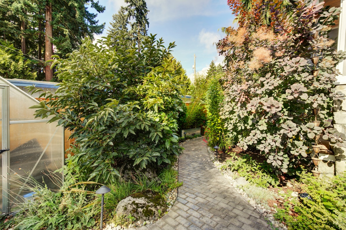 A charming pathway is framed by lush greenery and colorful foliage, leading to the entrance of the apartment. Soft lighting along the path highlights the natural landscaping, creating an inviting atmosphere for guests as they approach the entrance.