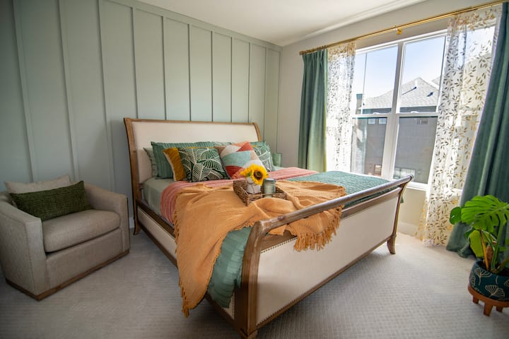 This gorgeous second bedroom is bright and colorful with a custom board and batten wall, gold-accent sheer curtains, green velvet drapes for privacy, and a comfortable King bed that you won't want to get out of.