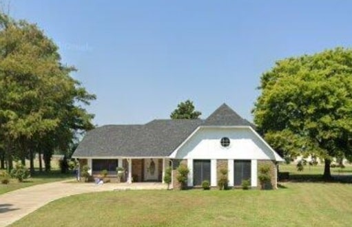 The exterior of the home is showcased, featuring a contemporary design with a steeply pitched roof and an inviting front porch. A spacious driveway leads to the entrance, surrounded by lush greenery and well-maintained landscaping, under a clear blue sky.