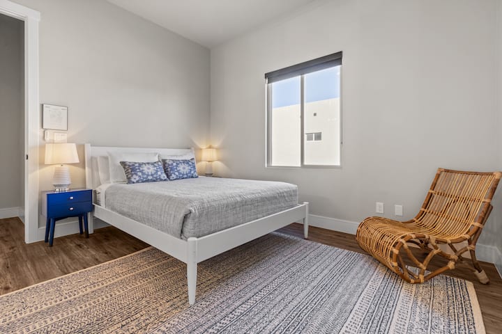 Un lit Queen Size confortable est habillé de draps blancs impeccables et complété par une chaise d'accent de bon goût et des meubles minimalistes, assurant un espace fonctionnel mais serein pour des nuits reposantes.