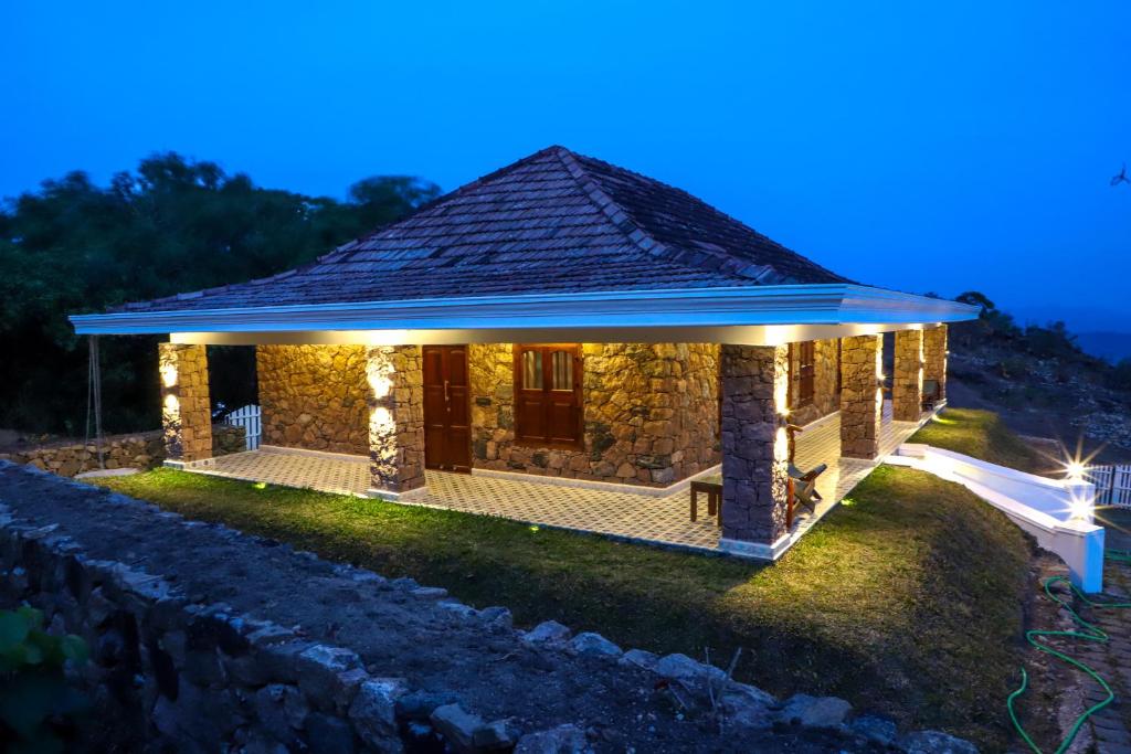 The stone villa is elegantly illuminated at dusk, showcasing a traditional architecture with a sloped roof. The spacious outdoor area features a paved pathway and soft lighting, enhancing the natural stone facade and inviting atmosphere around the property.