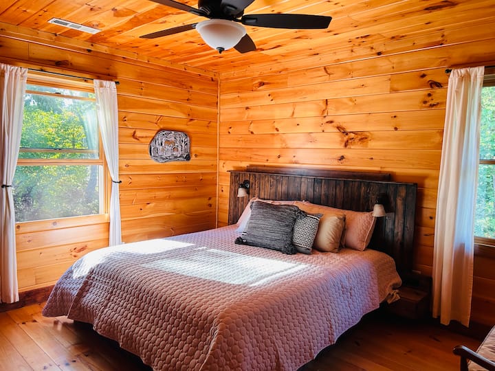 The top level has two bedrooms. This one has a king bed, dresser, smart TV, arm chair, bench, and local art. 