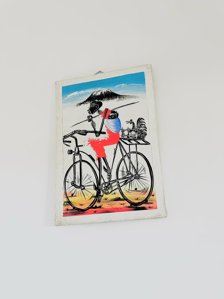 A colorful artwork is displayed on the wall, featuring a figure riding a bicycle. The figure is depicted in vibrant colors, accessorized with various items in a basket. The background presents a scenic landscape with a blue sky and distant mountains.