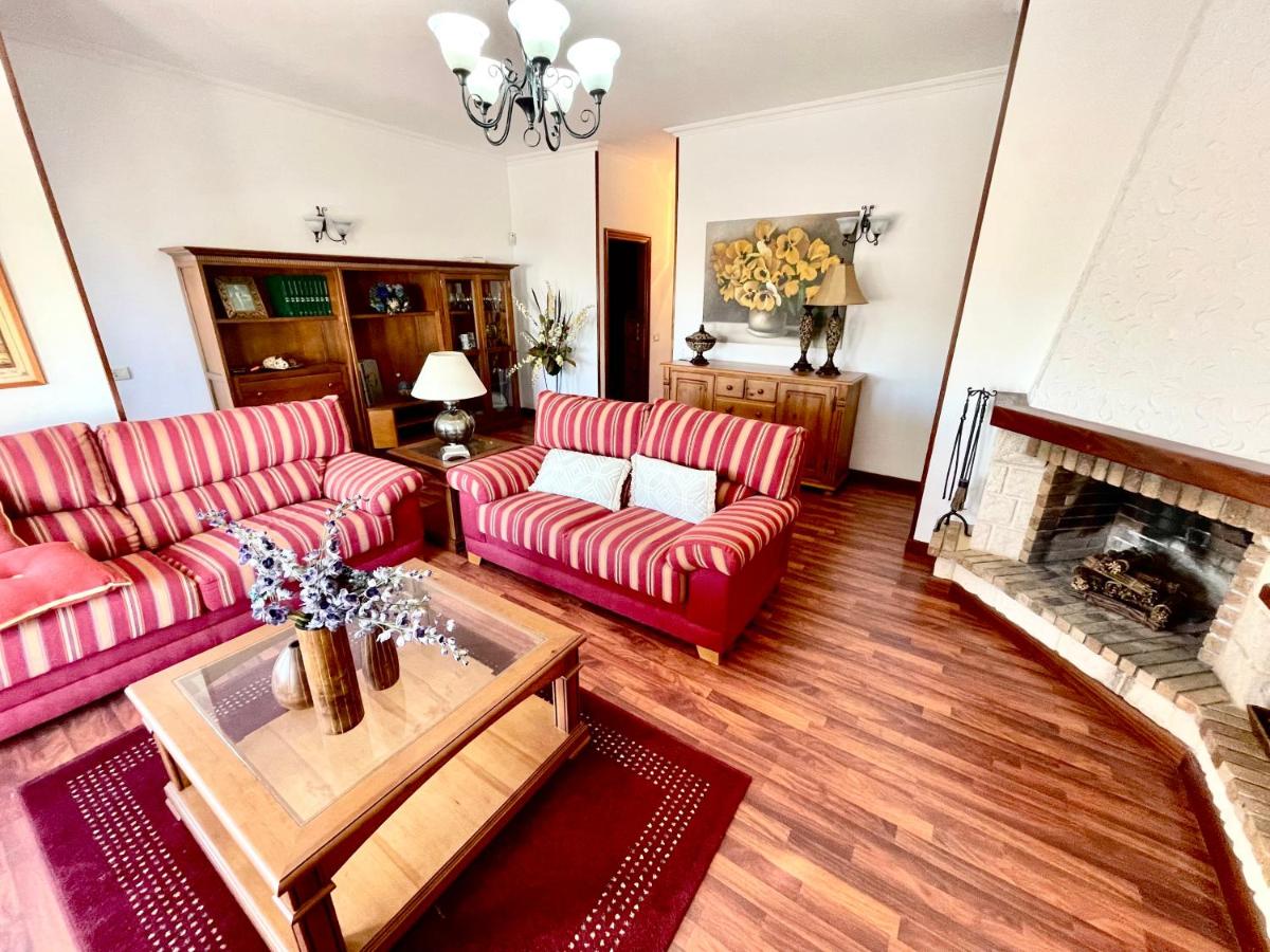 A comfortable living area displays two red-striped sofas complemented by light-colored cushions. A wooden coffee table sits in the center, adorned with a decorative arrangement. A fireplace is present, alongside a wooden cabinet and a shelf with decorative items, enhancing the inviting ambiance.