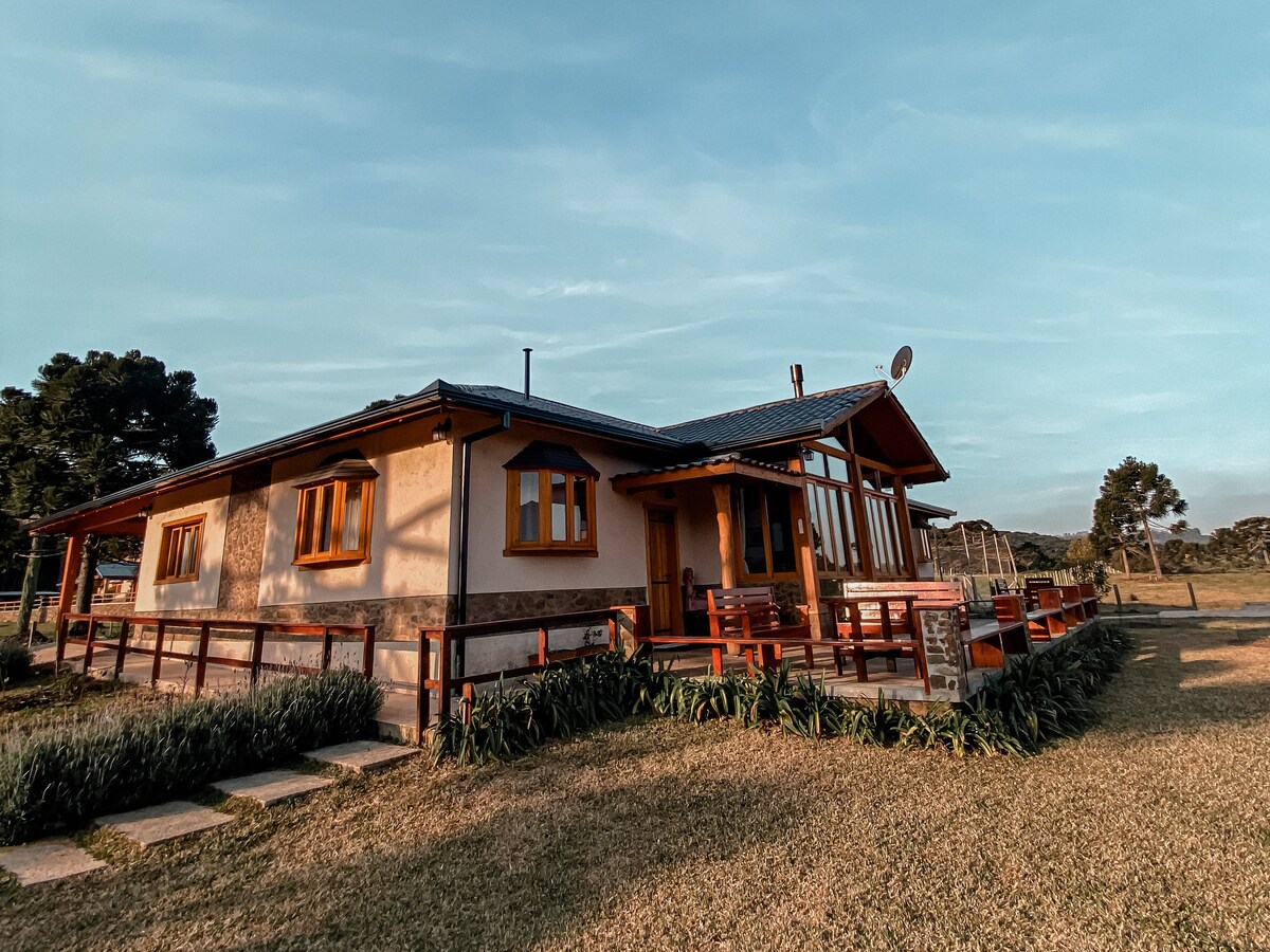 The charming cabin is framed by neatly trimmed grass and features a wooden deck. Large windows provide plenty of natural light, while the entrance is enhanced by a covered porch. Surrounding trees create a serene atmosphere in the countryside.