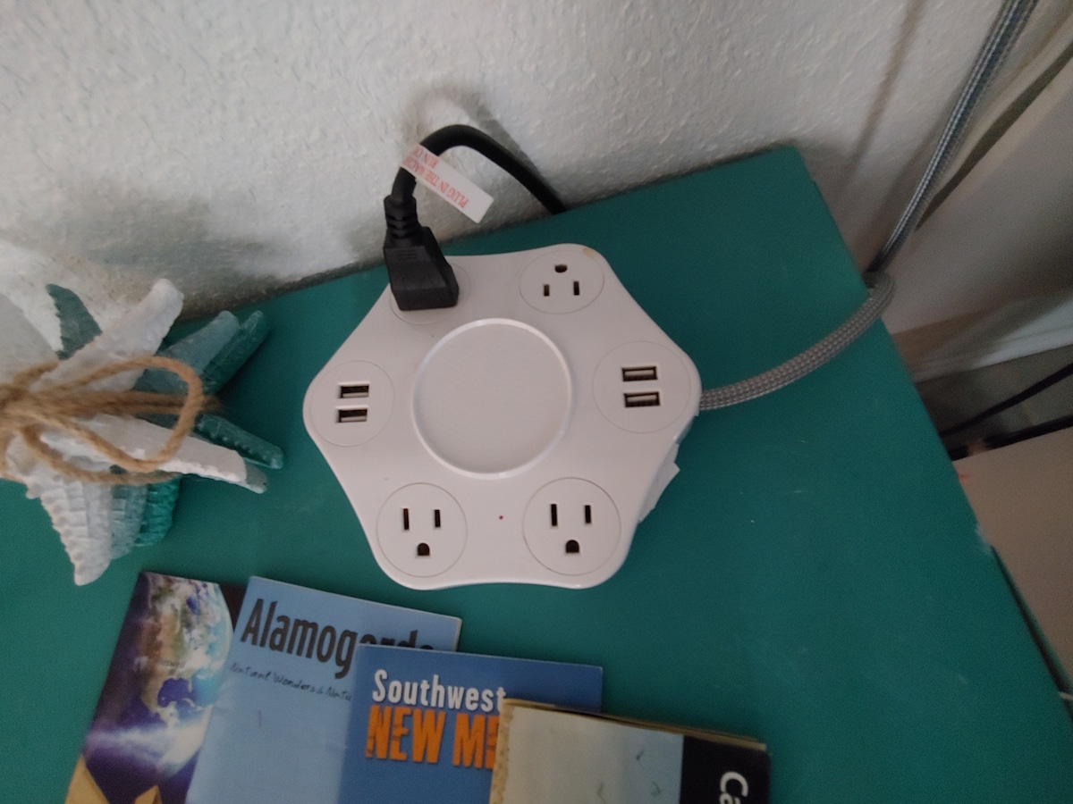 A power strip is located on a turquoise surface, featuring multiple standard outlets and USB ports for charging devices. Nearby, travel brochures and local guides are arranged, providing information about attractions in the area.