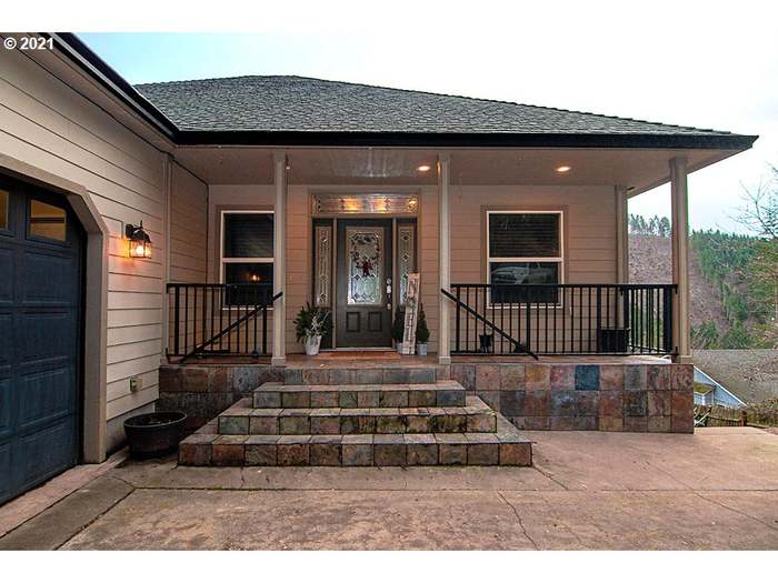 The entrance features a covered porch with a symmetrical layout, flanked by decorative plants. Stairs lead up to an elegant front door, while stone steps and a patterned patio provide a welcoming transition to the home.