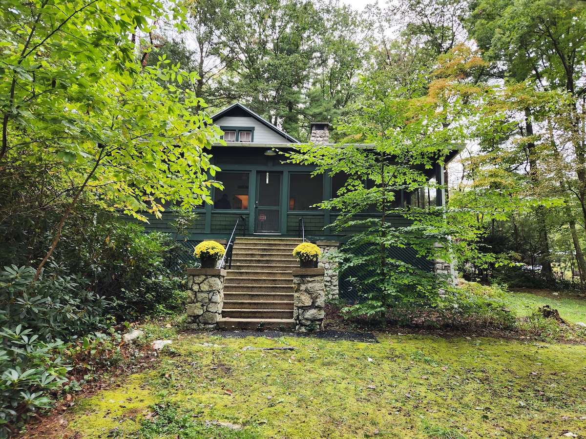 The home is set amidst greenery, with a stone staircase leading to the entrance. Yellow flowers are placed on either side of the steps. Surrounding foliage adds a natural touch, creating a serene entrance to the property.